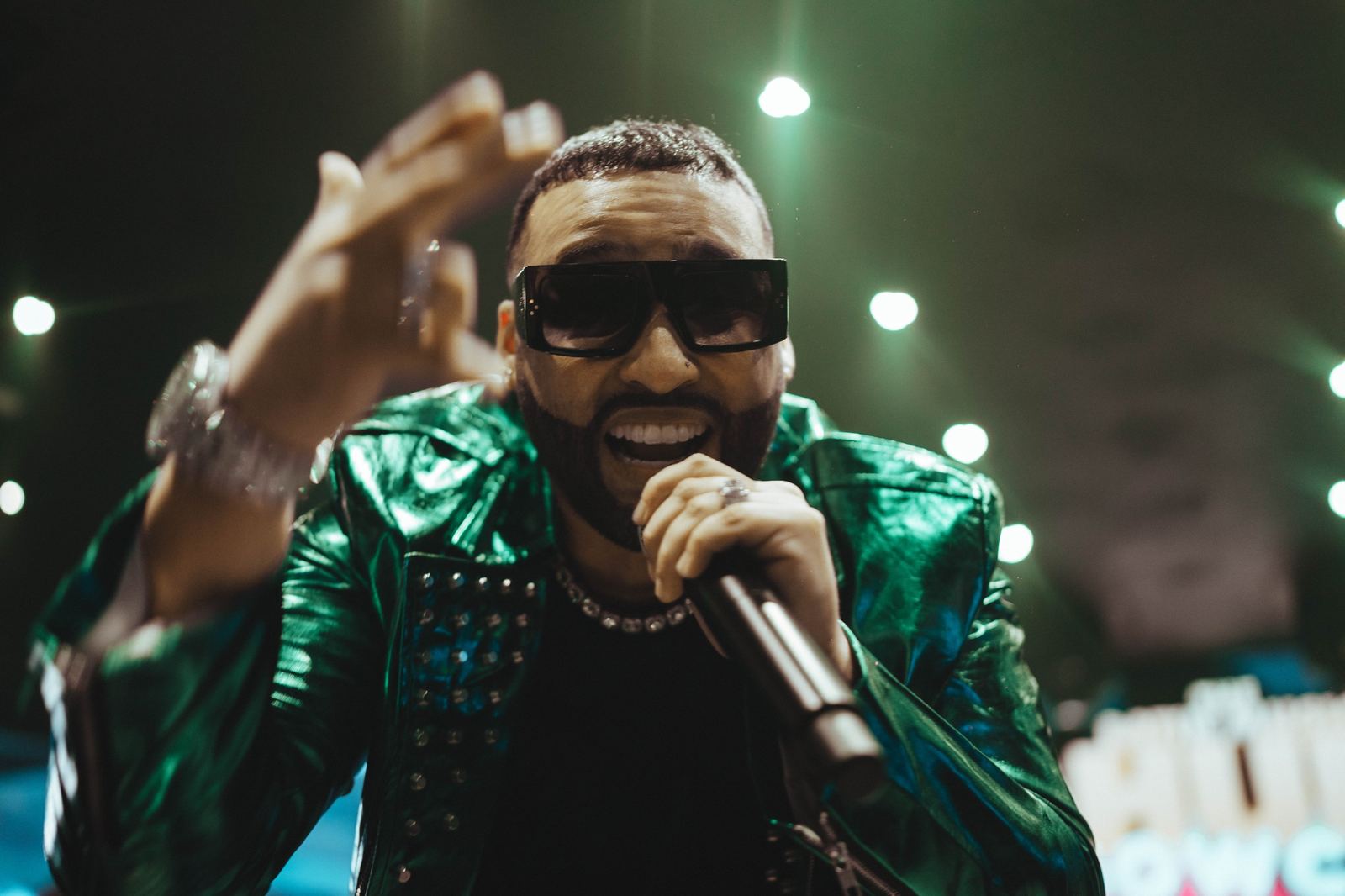A performer in a green leather jacket singing toward the crowd